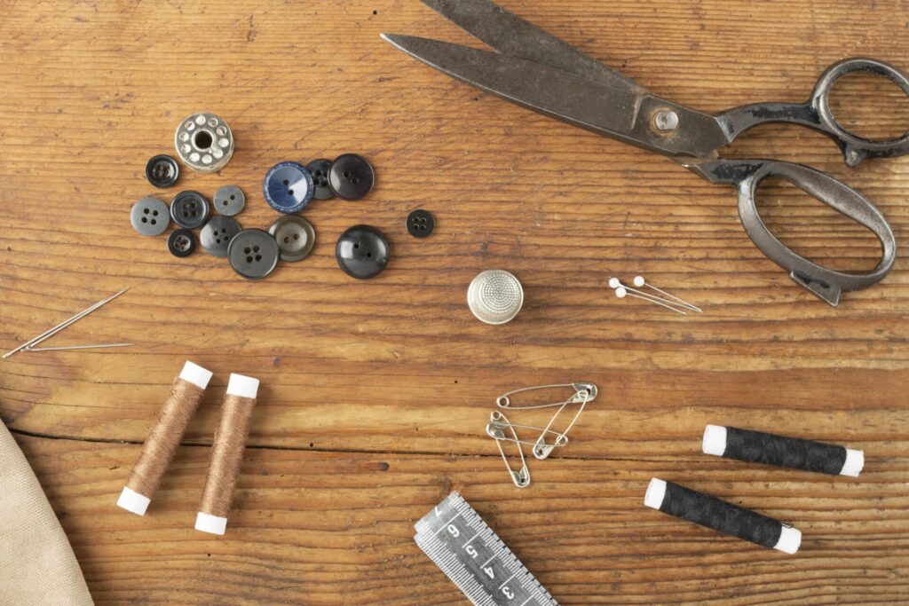 Vue d'un dessus de table en bois avec une paire de ciseau de couture, des boutons de toutes tailles et des fils de couleurs différents